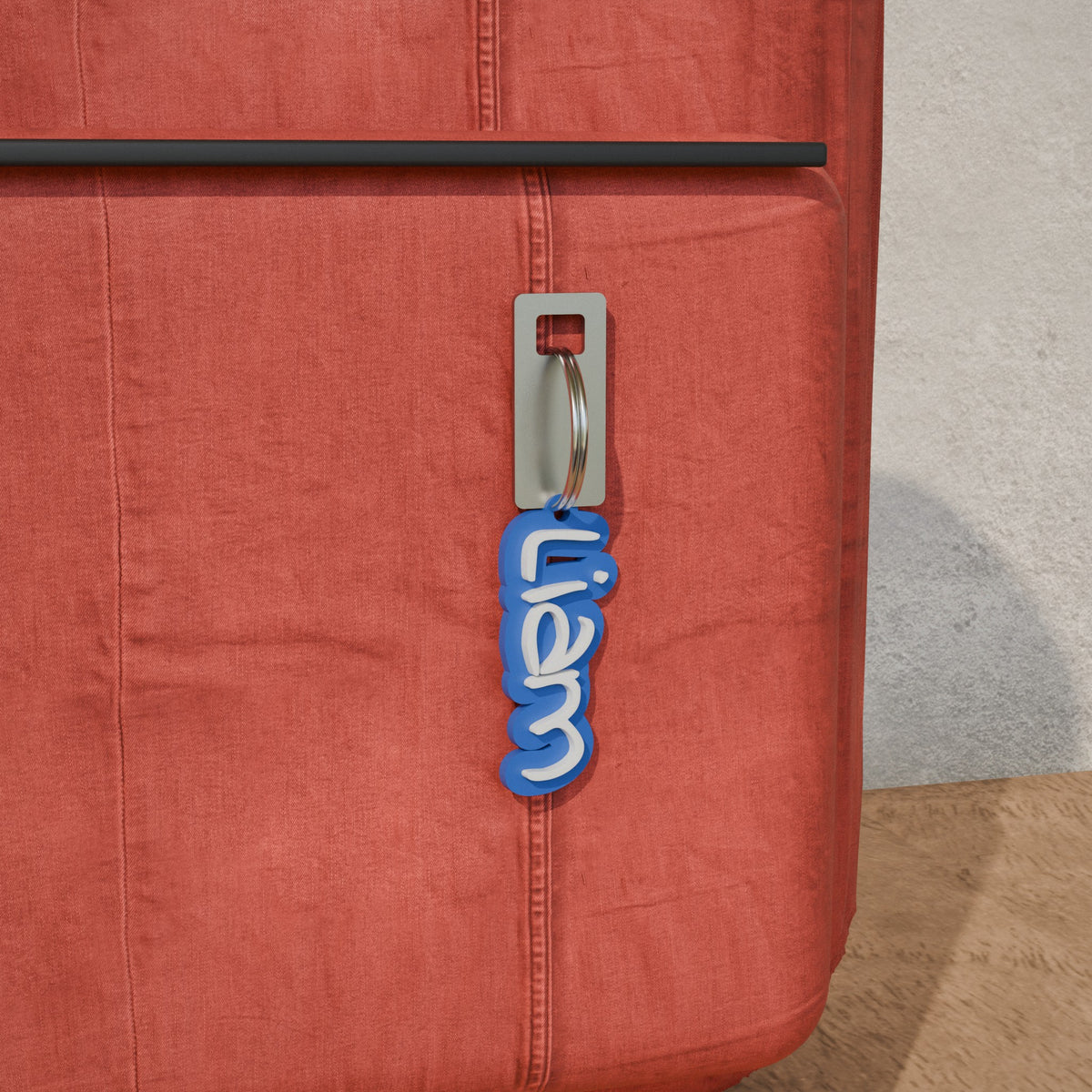 Blue and white Liam name keyring clipped to the zip of a red school bag