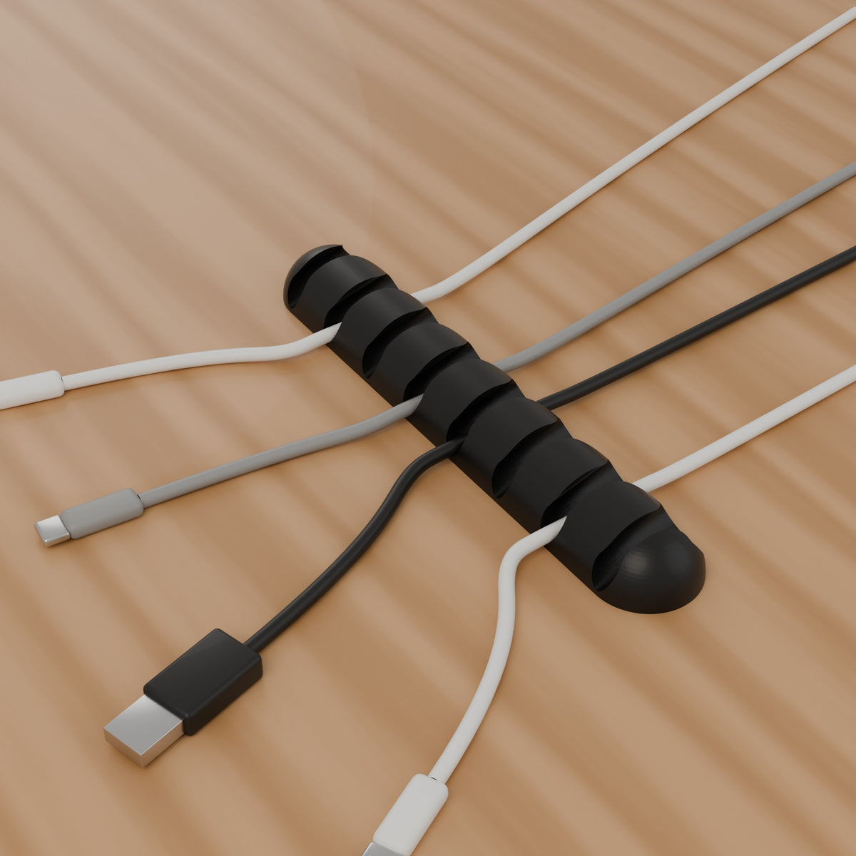 Black cable organiser holding charging cables on a desk
